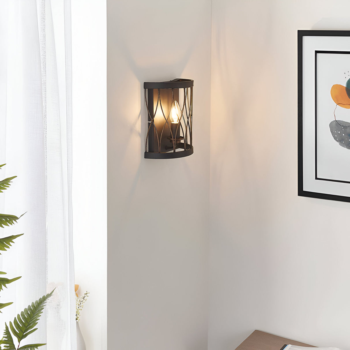 Endon Hulton wall light in matt black and rustic bronze with curved steel cage and E14 candle bulb, mounted in a corner beside framed art and sheer curtains.