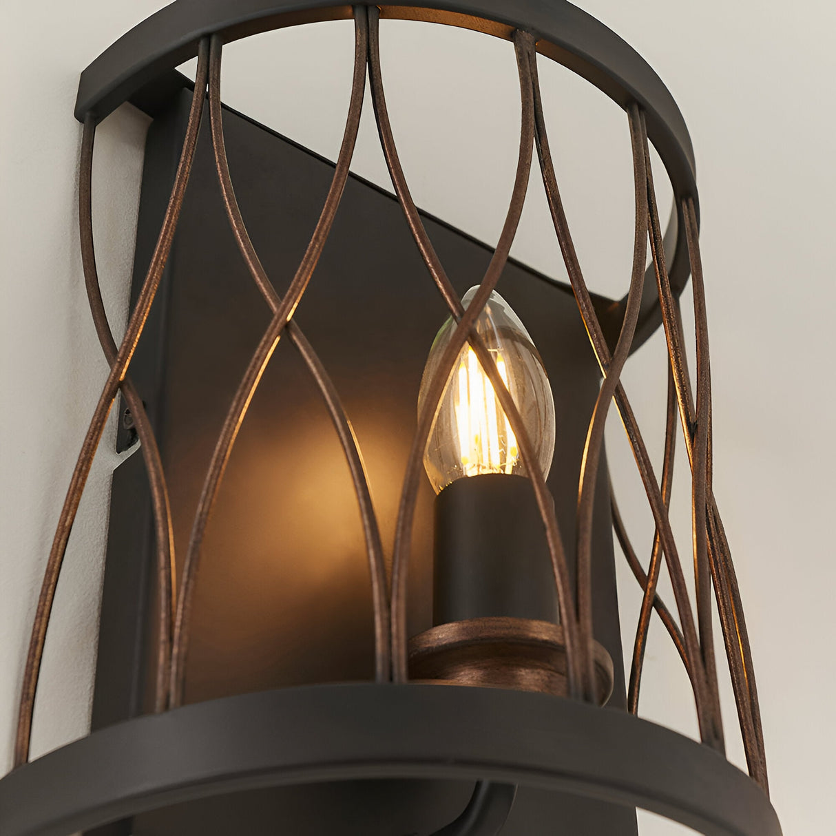 Close-up of Endon Hulton wall light showing lit E14 candle bulb within a matt black and rustic bronze steel cage with curved lattice detail.