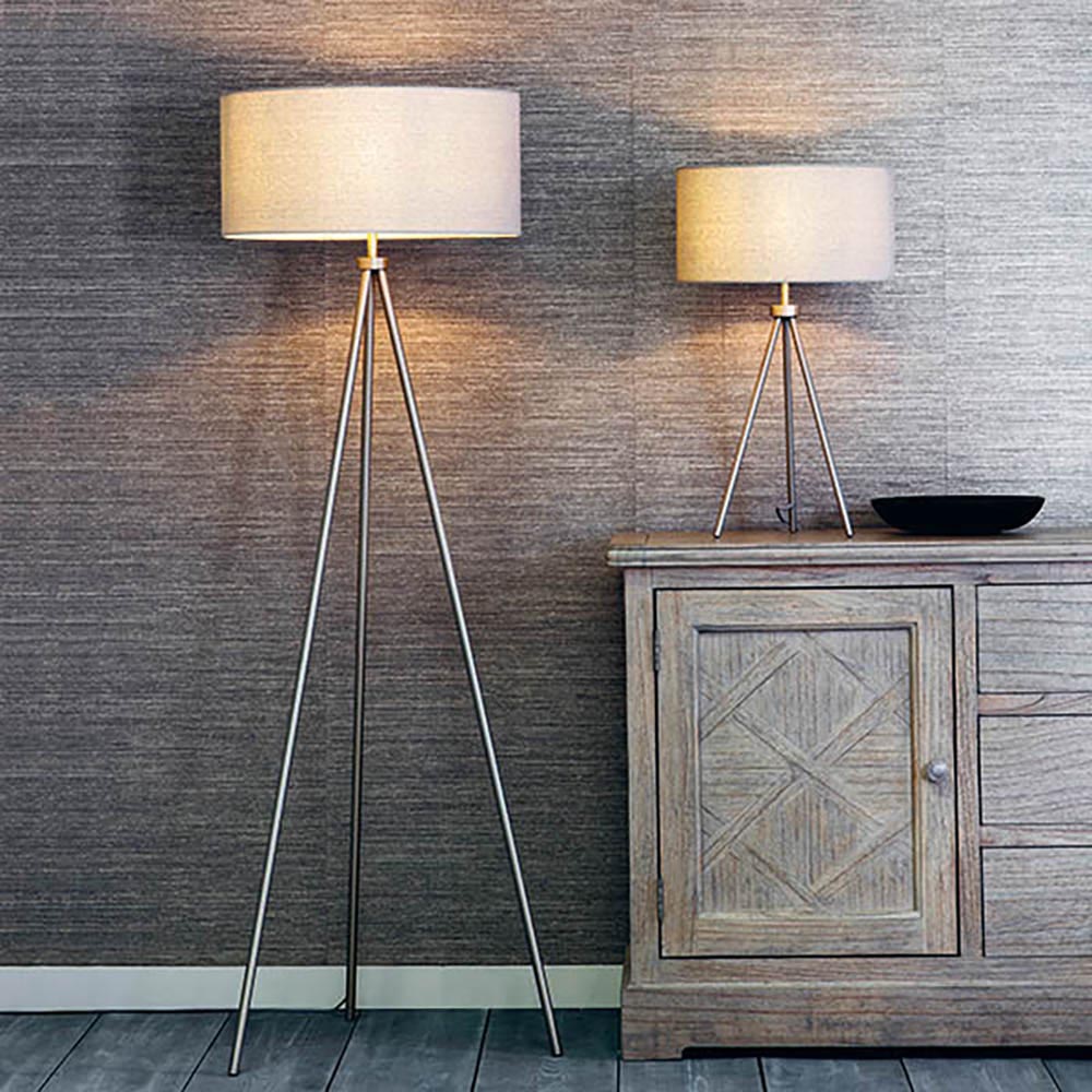 Endon Cranwell floor lamp with a nickel tripod frame and grey linen drum shade, shown beside a matching table lamp on a carved wood sideboard.