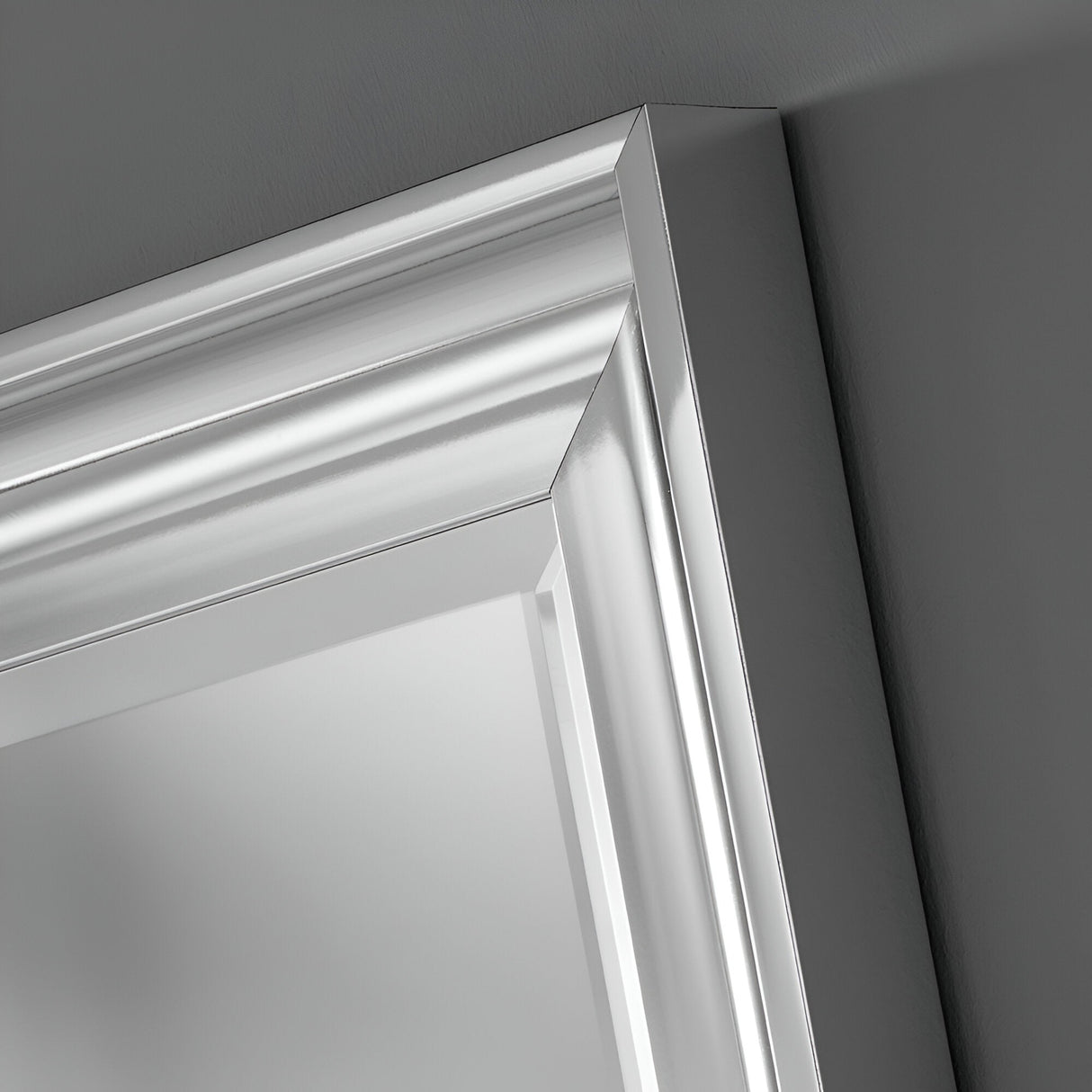 A close-up of the Wave Rectangle Wall Mirror - Silver reveals a metallic silver frame with reflective surfaces and beveled edges against a gray wall. This mirror enhances the clean, sharp lines, providing a modern and sleek appearance ideal for any contemporary living space.