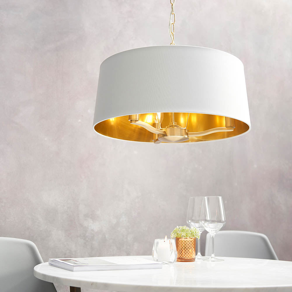 Endon Brendale 3 light pendant with white faux silk drum shade and metallic gold inner lining, hanging from a gold chain above a marble dining table.