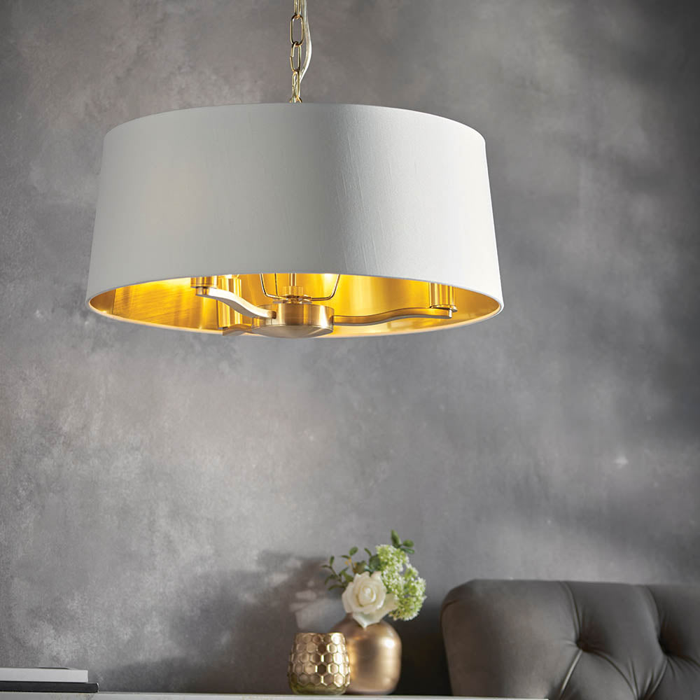 Endon Brendale 3 light pendant with a white faux silk drum shade and metallic gold inner lining, hanging above a console with roses in a living room.