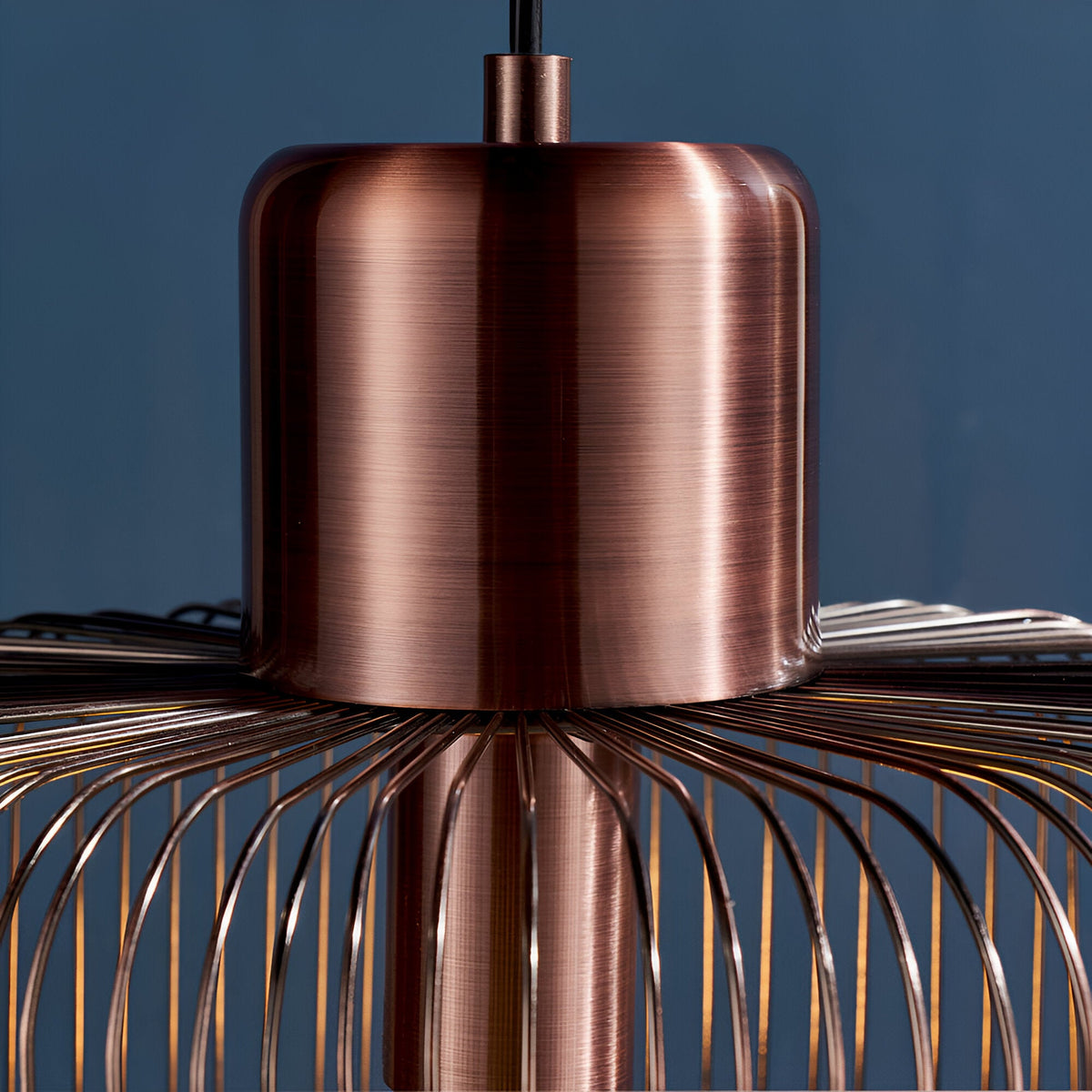 Castdale Cage Pendant in antique copper, close-up of the cylindrical metal fitting with wire cage frame, on black flex against a dark blue background.
