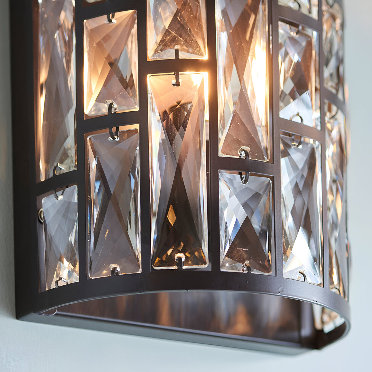 Close-up of Endon Aldwick wall light showing tiered faceted clear crystals in a dark bronze metal frame, illuminated by a warm E14 bulb.