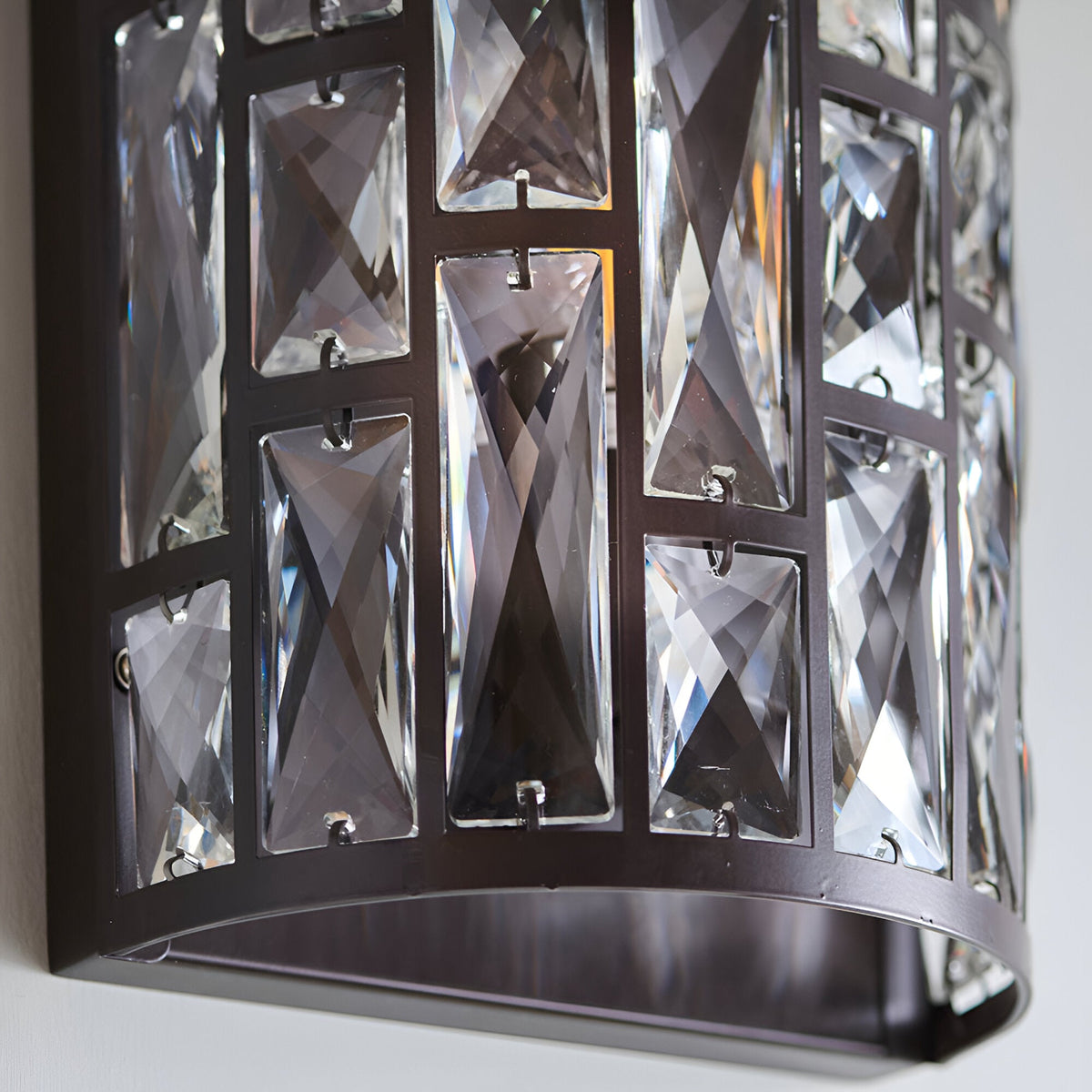 Close-up of Endon Aldwick wall light in dark bronze, showing tiered faceted clear crystals set in a rectangular metal frame against a pale wall.