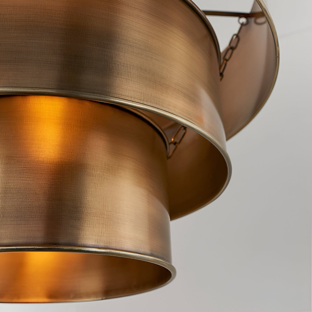 Close-up of the Endon Carlwick tiered pendant showing stacked cylindrical shades in aged brass with a lit interior glow and chain suspension.