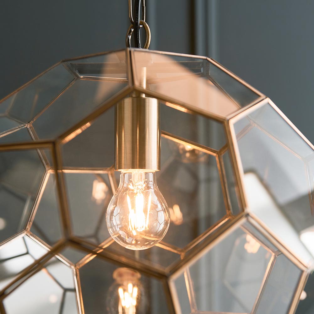 Endon Carldon Hexagonal Pendant in antique brass, close-up of the geometric clear glass panels, brass edging, lit E27 bulb and chain suspension.