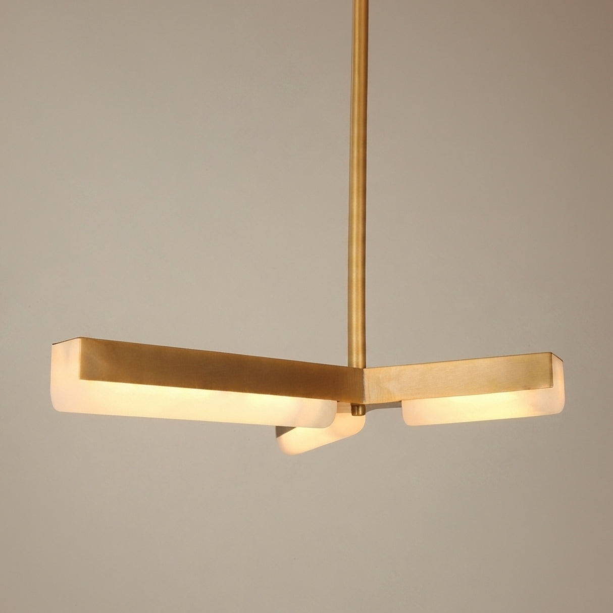 Elvaris LED Radial Alabaster Chandelier in brushed brass, three angular arms with alabaster diffusers glowing warm white, suspended from a slim rod against a plain light background.
