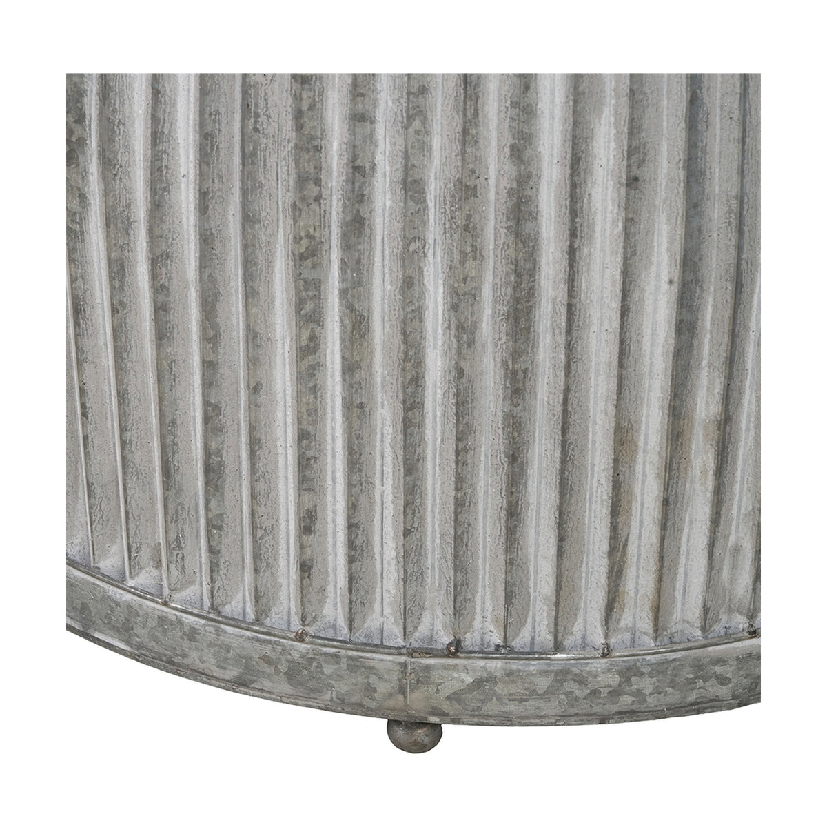 Close-up of a galvanised zinc barrel planter, showing ribbed vertical fluting, weathered metal finish, and a small ball foot on a plain background.