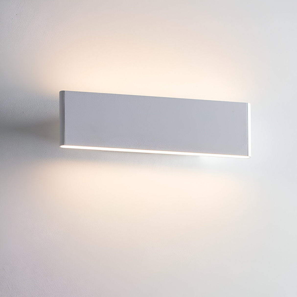Endon Ambrose matt white LED wall light, compact rectangular fitting casting warm up-and-down glow on a pale wall.