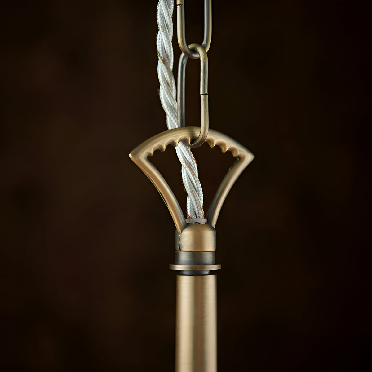Close-up of the Endon Castwell pendant's antique brass suspension loop, chain link, and grey twisted fabric flex against a dark background.