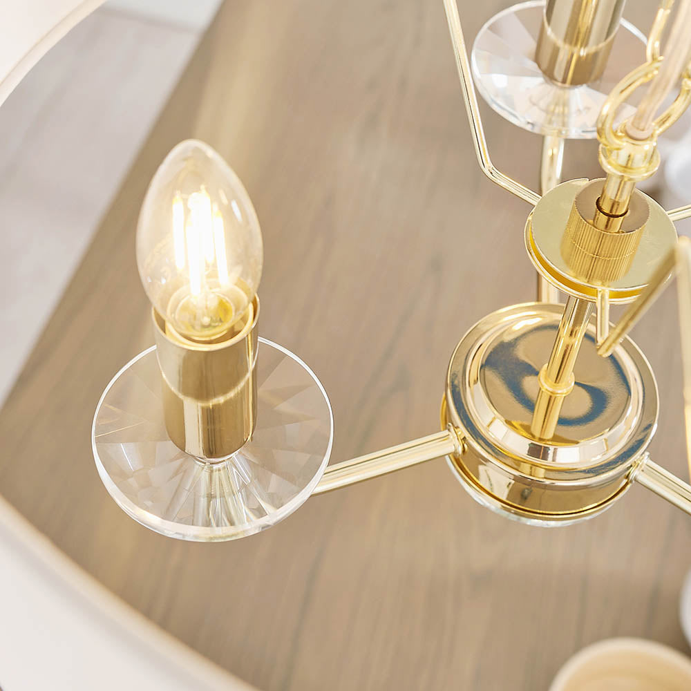 Close-up of the Endon Castdon 3 Light Pendant showing a brass arm with K9 crystal bobeche, E14 lit filament lamp, and central brass hub over a wood surface.