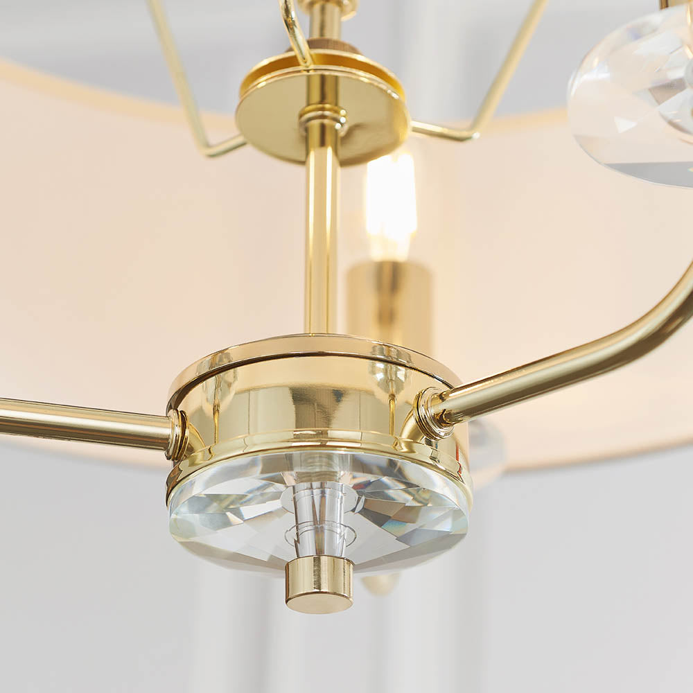 Close-up of the Endon Castdon 3 Light Pendant showing the brass central hub, K9 crystal bobeche detail, and edges of the white faux silk shades.
