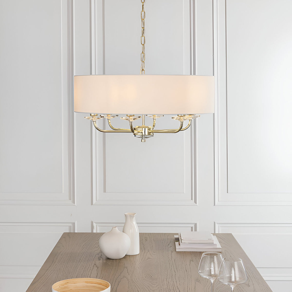 Endon Castdon 6 light pendant in brass with white drum shade and K9 crystal detail, suspended above a wooden dining table in a panelled room.