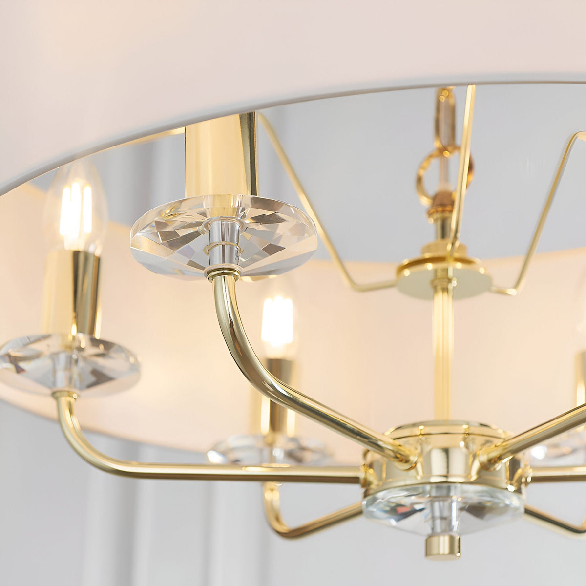 Close-up of Endon Castdon 6 Light Pendant in brass with white faux silk shade, showing curved arms, K9 crystal bobeches, and E14 candle lamps.