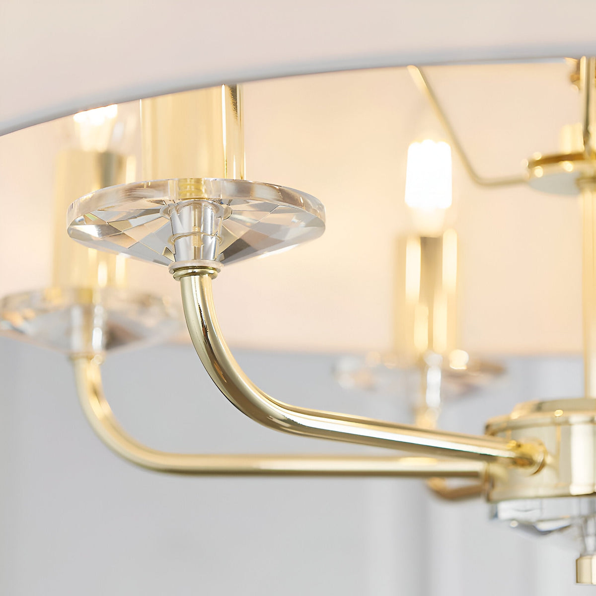 Close-up of Endon Castdon 6 Light Pendant in brass and white, showing a curved arm, K9 crystal bobeche, and lit E14 lamp beneath the faux silk shade.