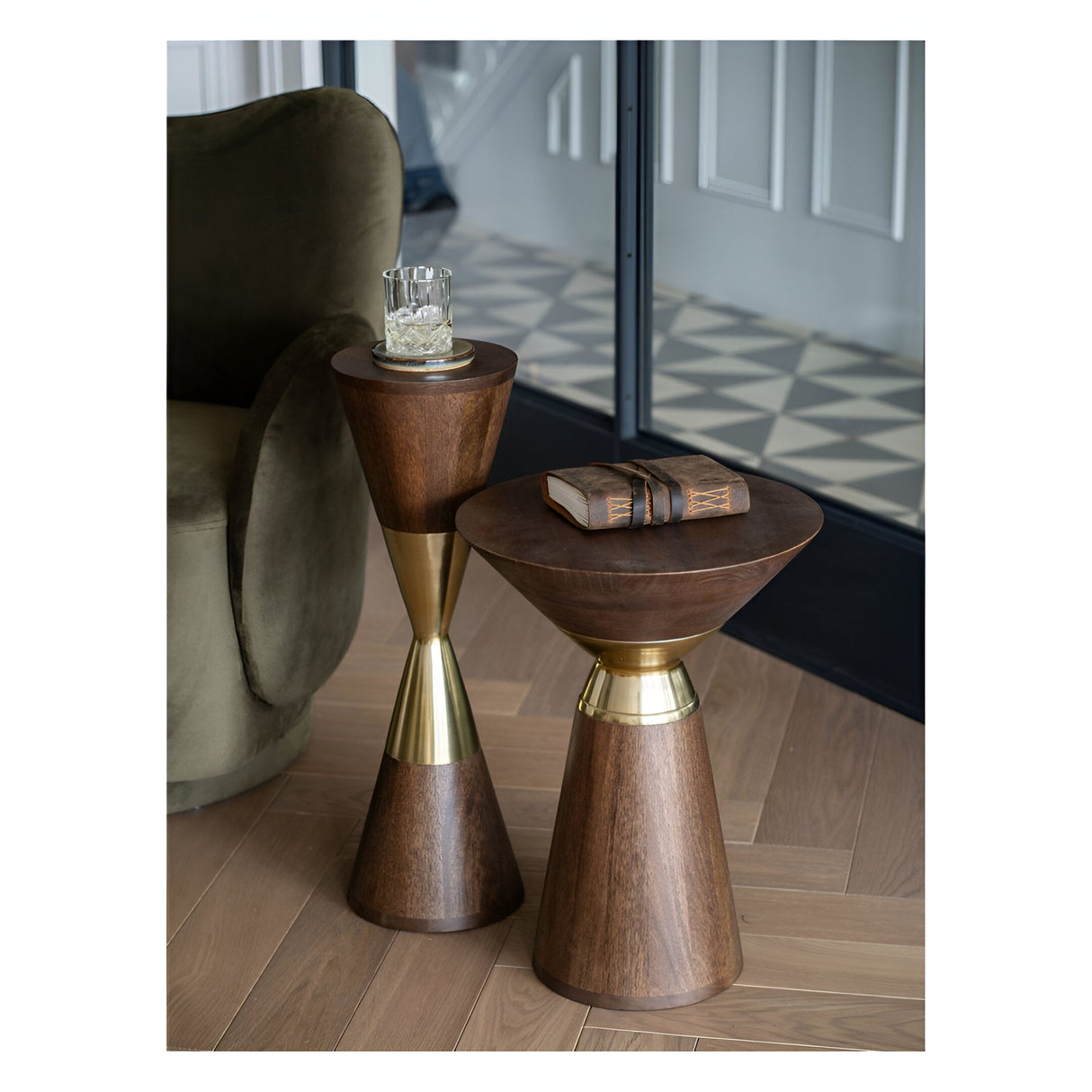 Libra Interiors Amalfi side tables in dark mango wood with brass-effect aluminium bands, styled beside a green velvet armchair on parquet flooring.
