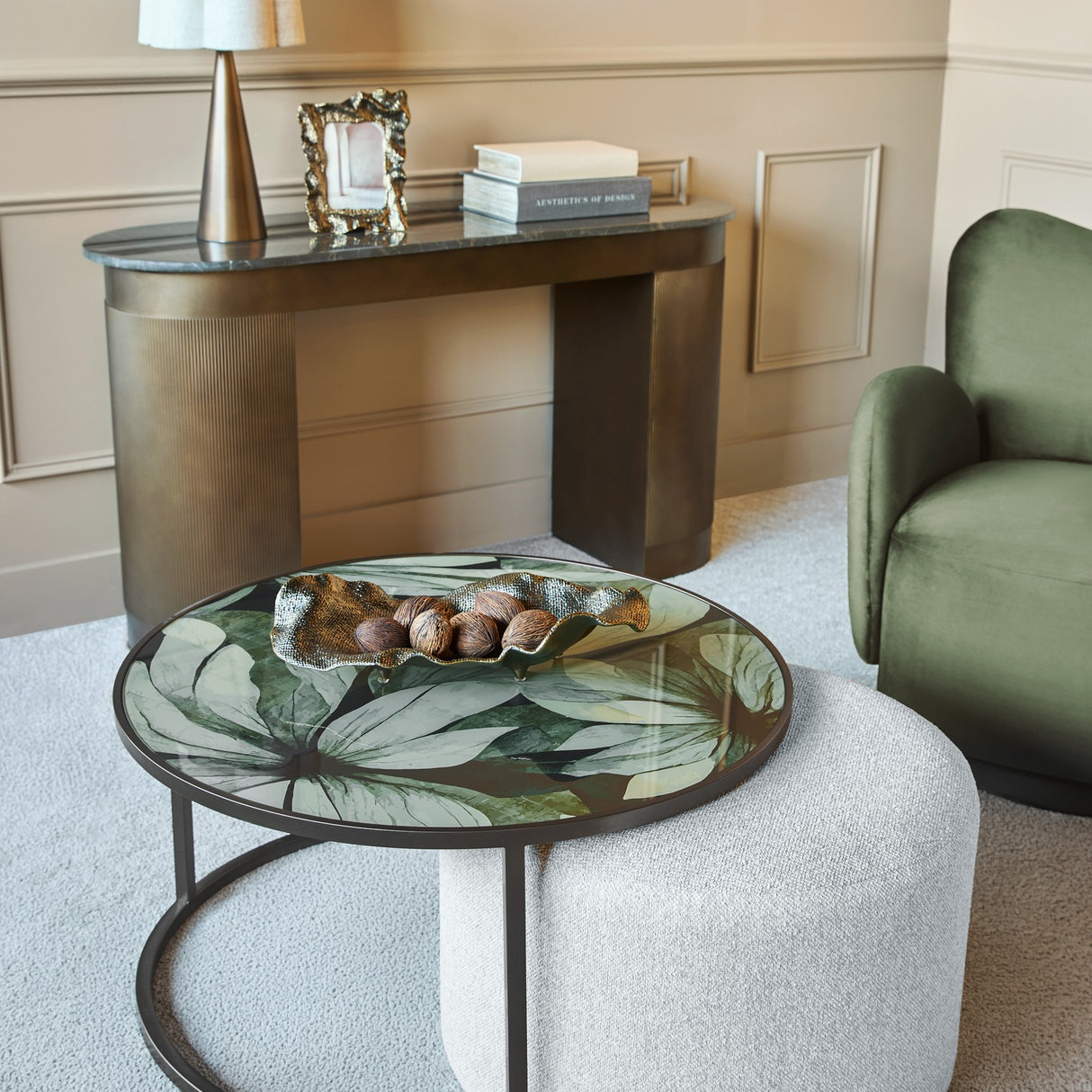 Libra Interiors Printed Glass Nesting Coffee Table in black with green leaf-print top on oatmeal pouffe, styled in a neutral living room with green armchair.