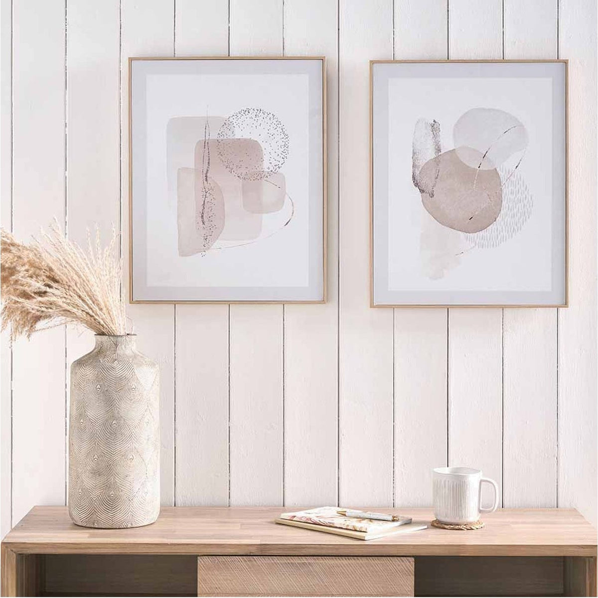 Set of 2 natural abstract canvas wall art prints in thin wood frames, shown above a wooden console table with a textured vase and white mug.