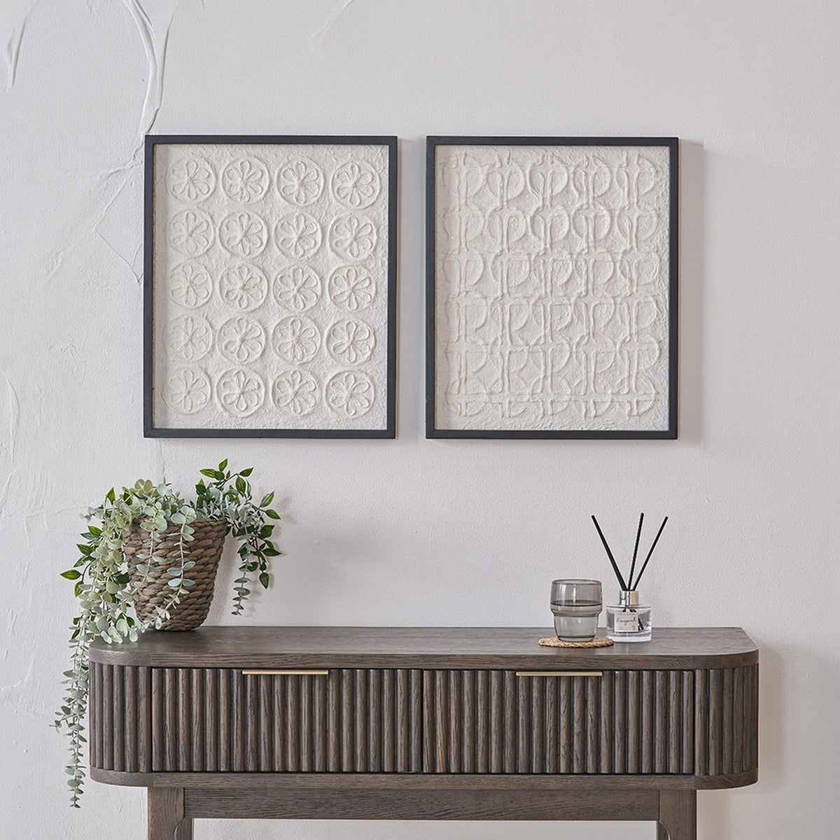 Set of 2 natural paper wall art panels with black frames, one featuring a floral grid pattern and the other a linear motif, displayed above a wooden console table.