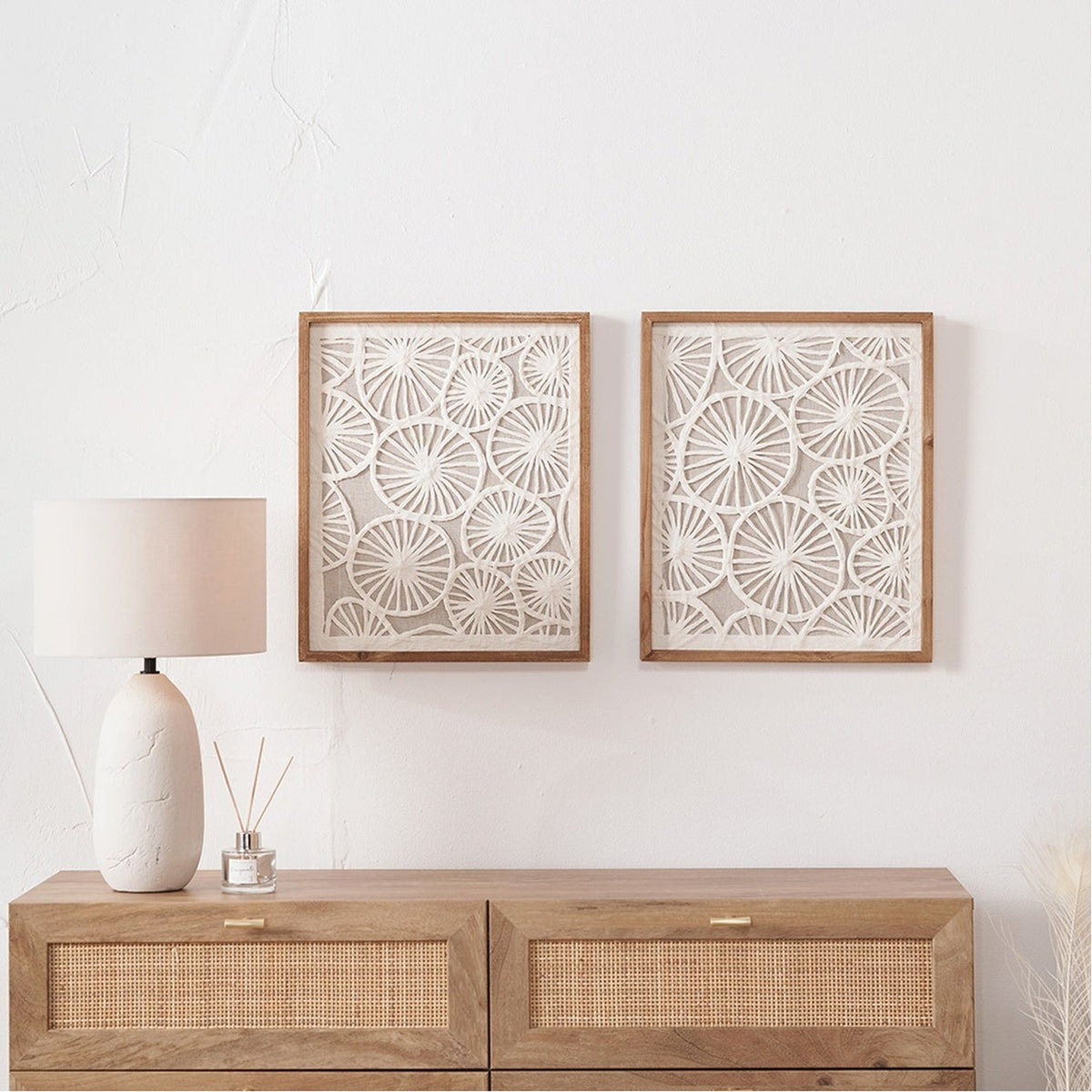 Set of 2 Cut Out Pattern Natural Paper Design Wall Art with wood frames, circular sunburst motifs, hung above a rattan-front sideboard in a neutral room.