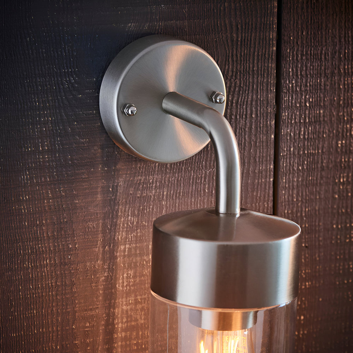 Endon Castfield outdoor wall light in brushed silver steel, close-up of the round wall plate and curved arm mounted on dark textured wood.