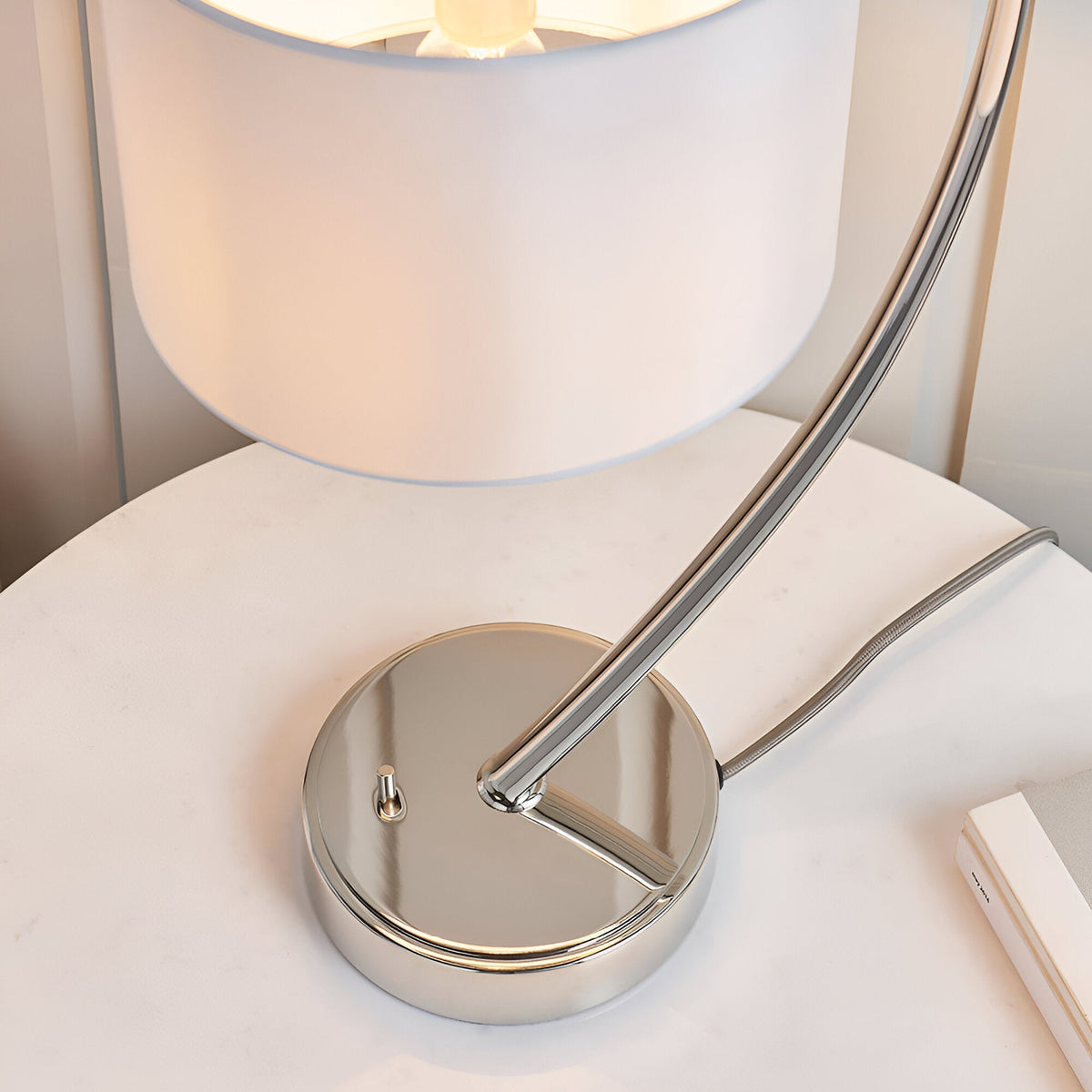 Brockfield Table Lamp in bright nickel finish, showing the curved arched stem, round base with toggle switch, and white faux silk shade.