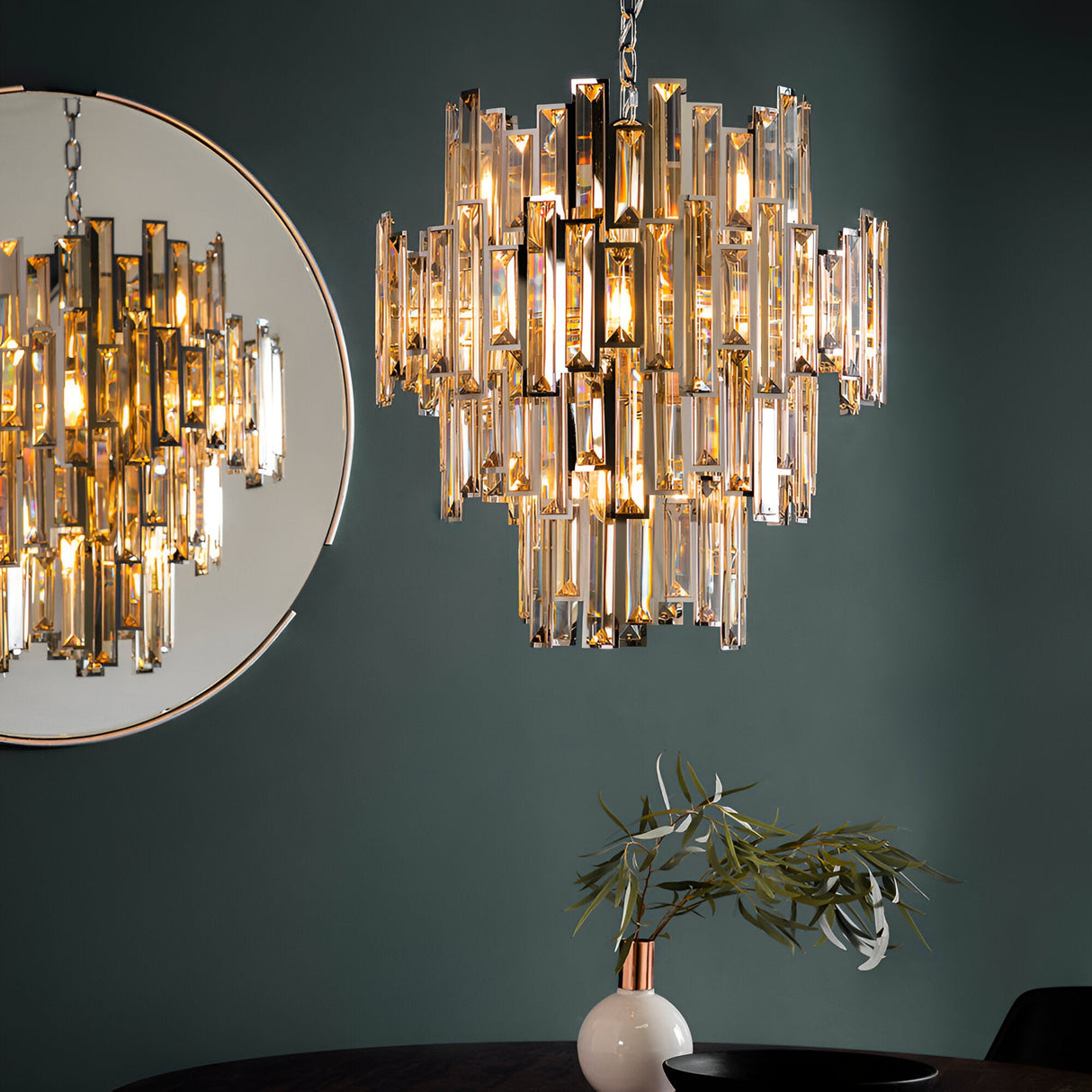 Endon Danedale 12 light chandelier in polished chrome with tiered champagne crystals, hung beside a round mirror against a dark green dining room wall.