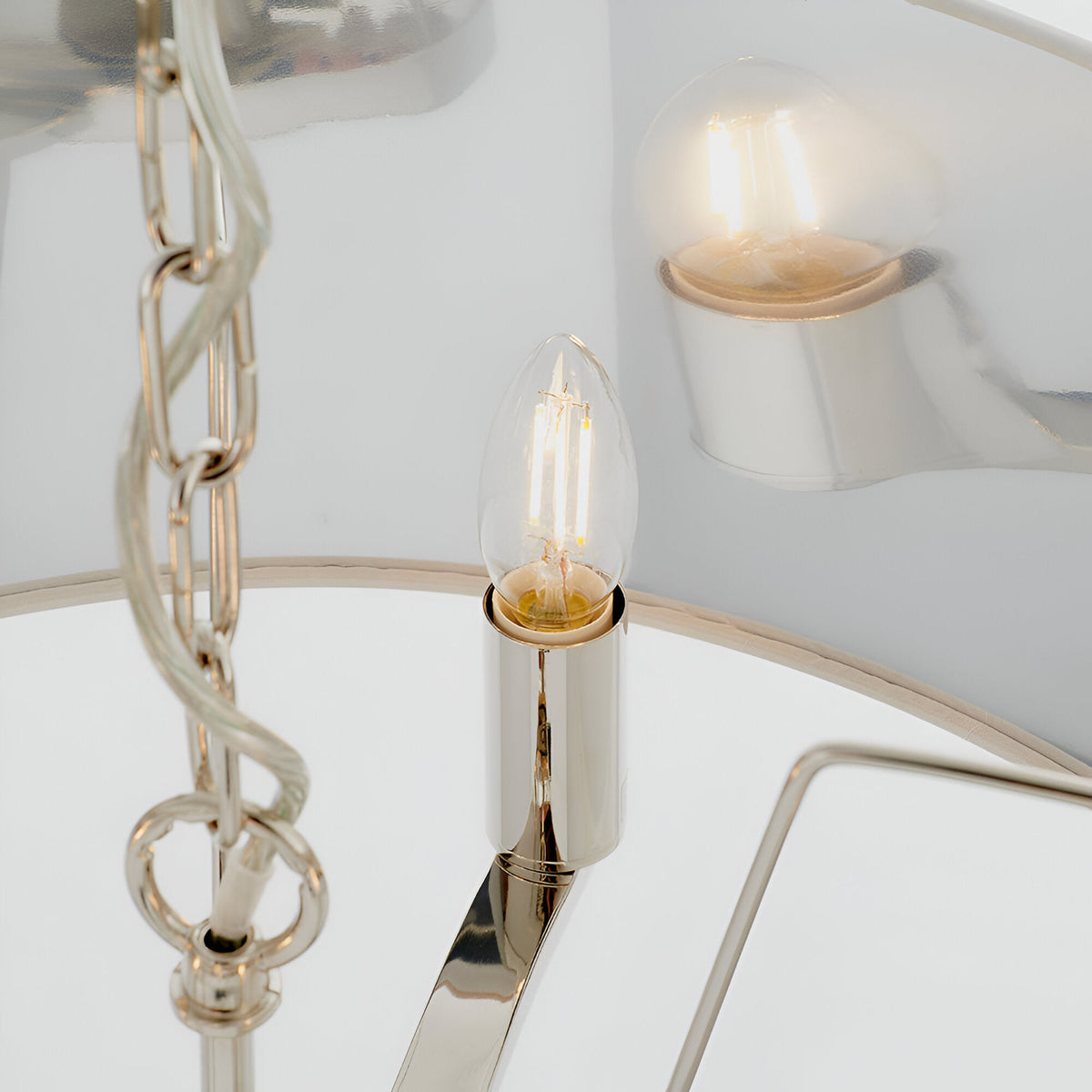 Close-up of the Endon Brendale 3 light pendant showing a nickel candle lamp holder, chain suspension and metallic silver-lined shade interior with lit bulbs.