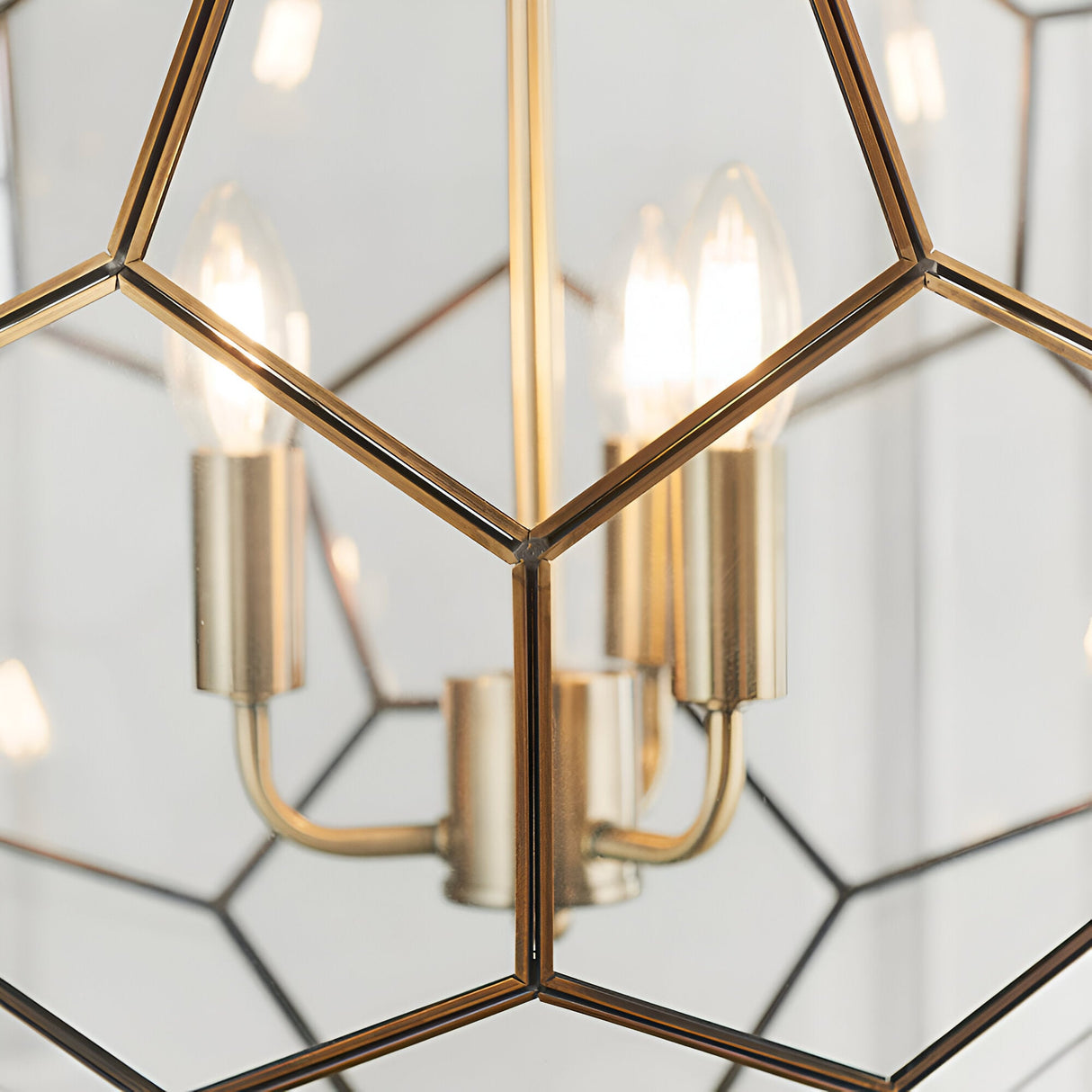 Close-up of Endon Carldon 3 Light Pendant showing antique brass candle-style lampholders, lit bulbs and hexagonal clear glass panels edged in brass.