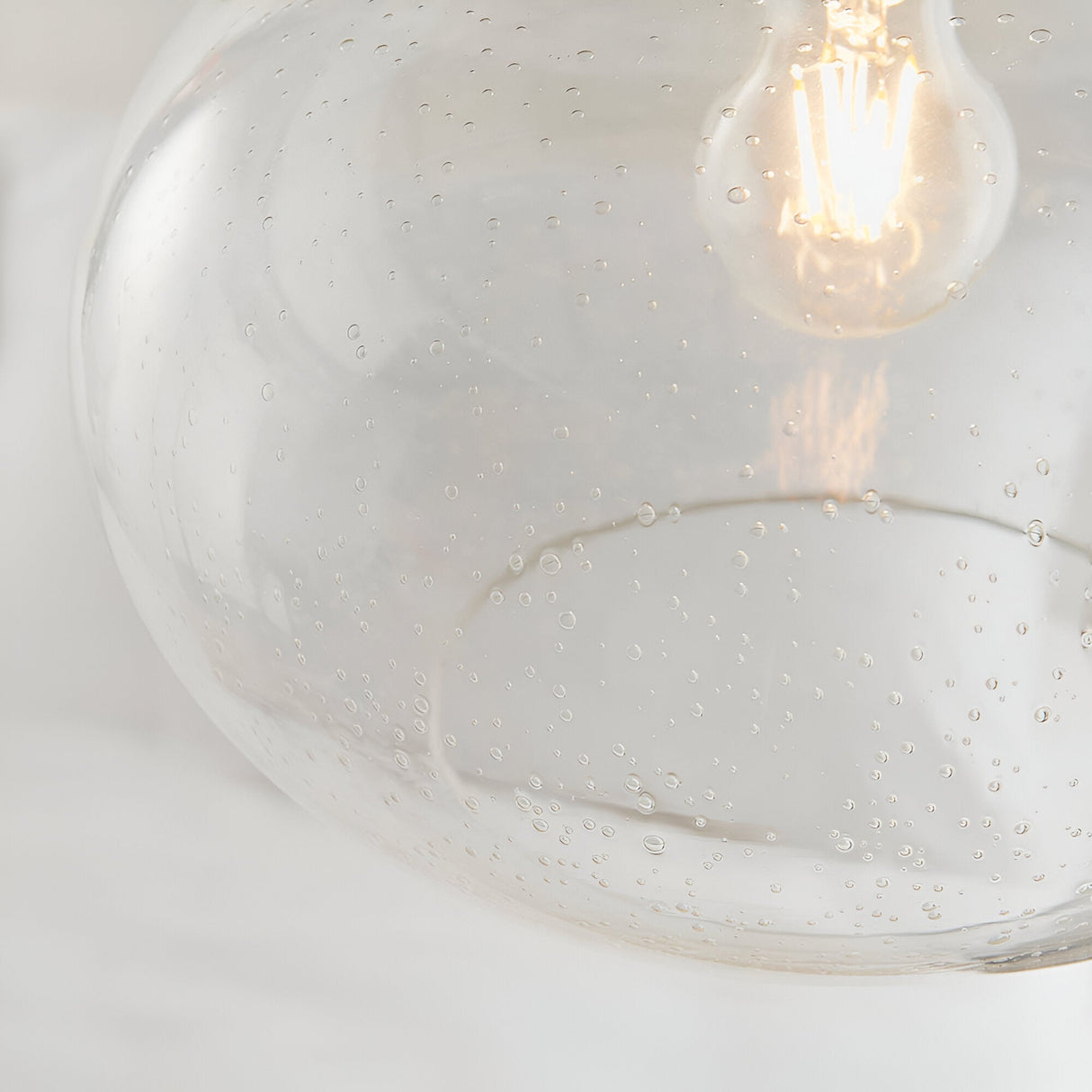 Close-up of Endon Brackcombe pendant shade in clear bubble glass with an exposed filament E27 lamp glowing inside.