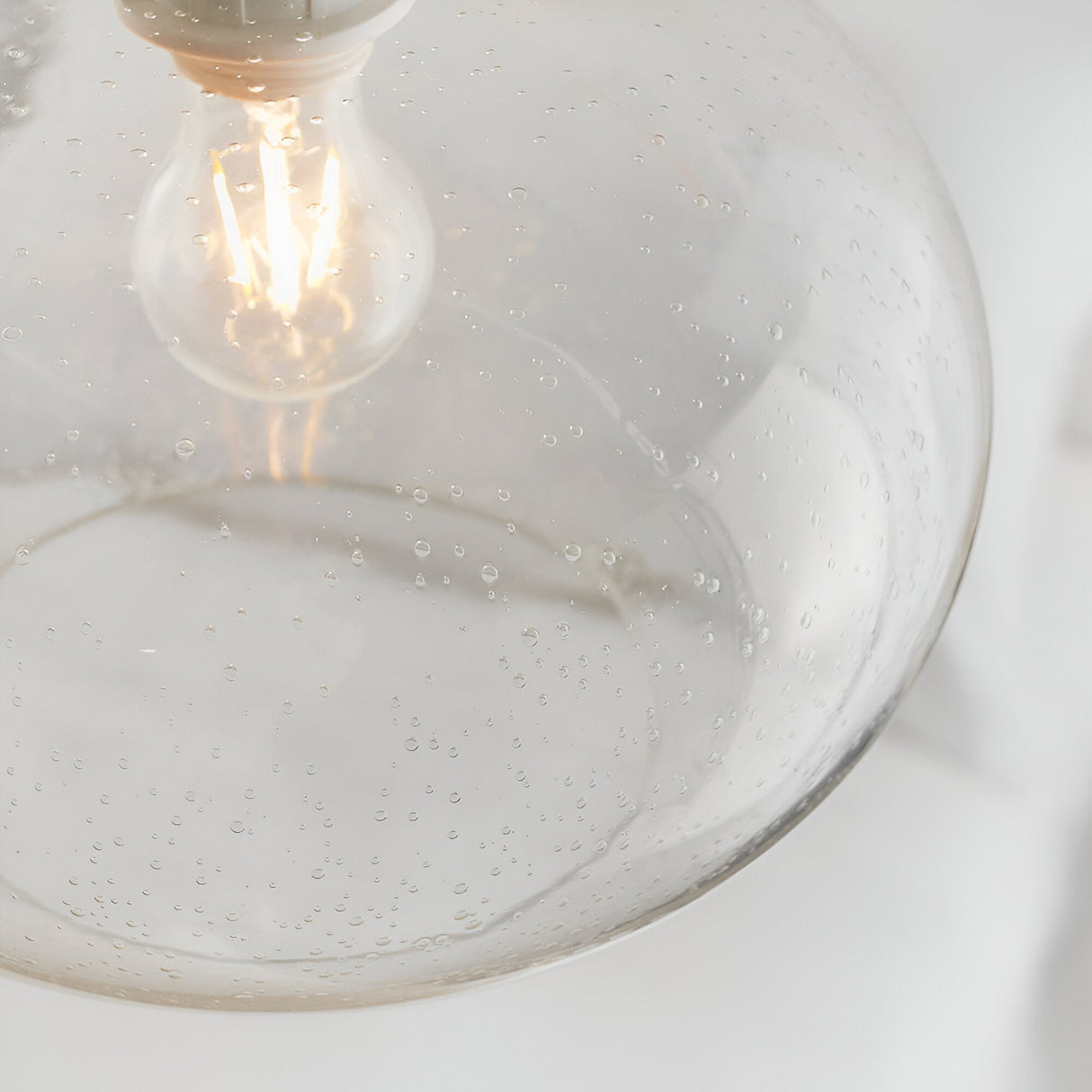 Close-up of the Endon Brackcombe clear bubble glass pendant shade with an exposed filament E27 lamp glowing inside the rounded globe.
