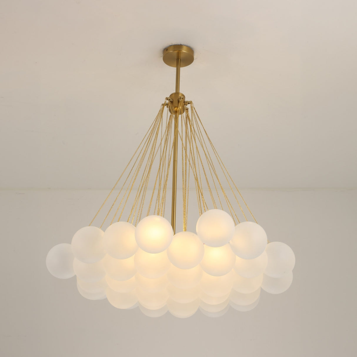 The Orb 37 Light Cluster Suspension - Gold features modern frosted glass globes clustered together, suspended by gold rods from a brass mount, adding striking elegance and brightness to a plain white ceiling.