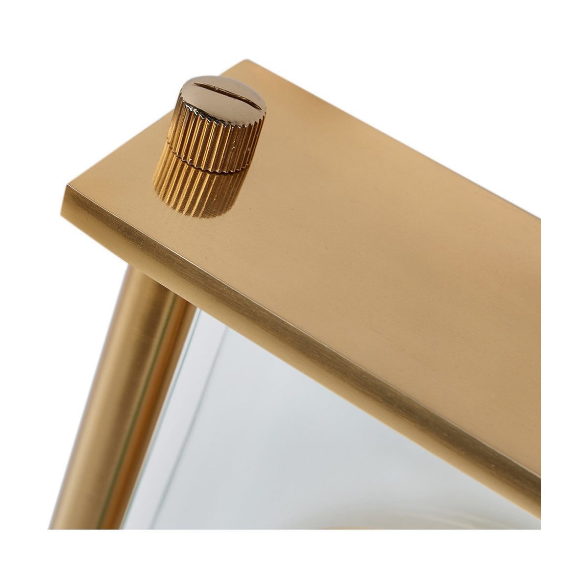 Close-up of the Gold Brass & Glass Floating Clock Face Table Clock, showing the gold metal top corner with a ridged winder knob and glass panel below, on a plain white background.