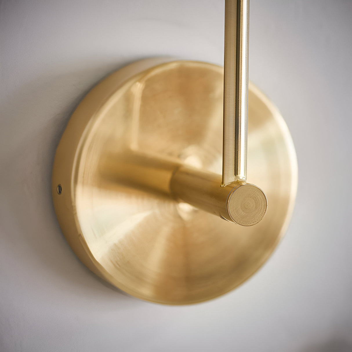 Close-up of the Endon Sinclair wall light's brushed brass circular backplate and cylindrical arm mounted against a pale wall.