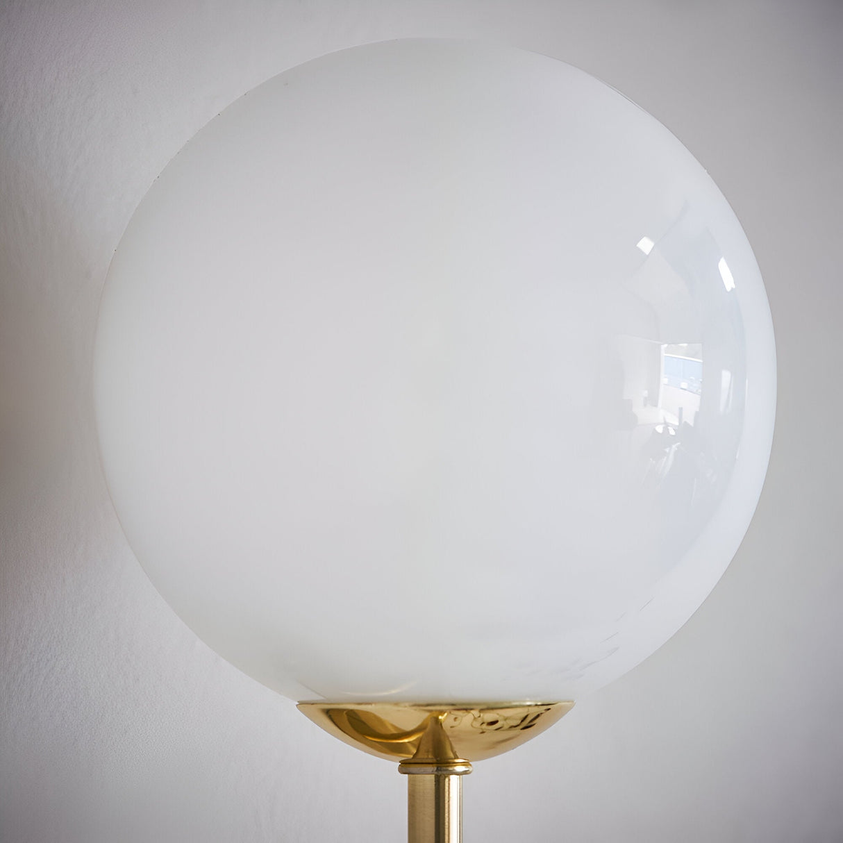 Endon Sinclair wall light with a large gloss opal blown glass globe shade on a brushed brass stem, shown against a plain white wall.