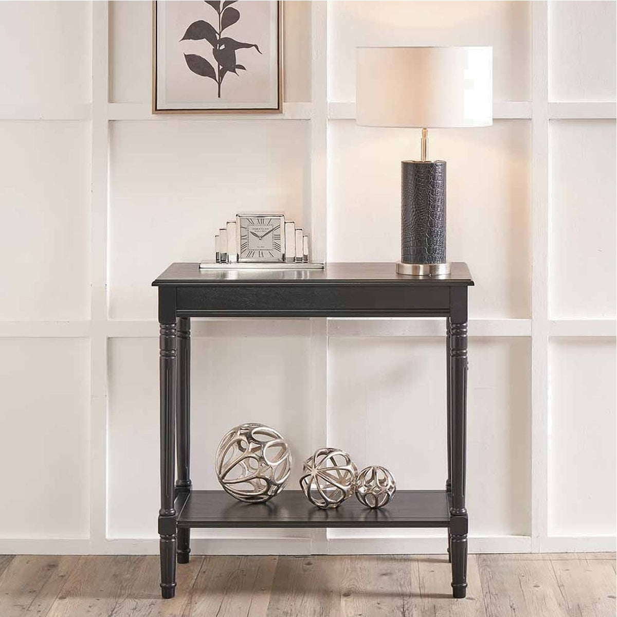 Heritage Black Pine Console Table with turned legs and lower shelf, styled in a hallway with a table lamp, clock, and decorative silver ornaments.