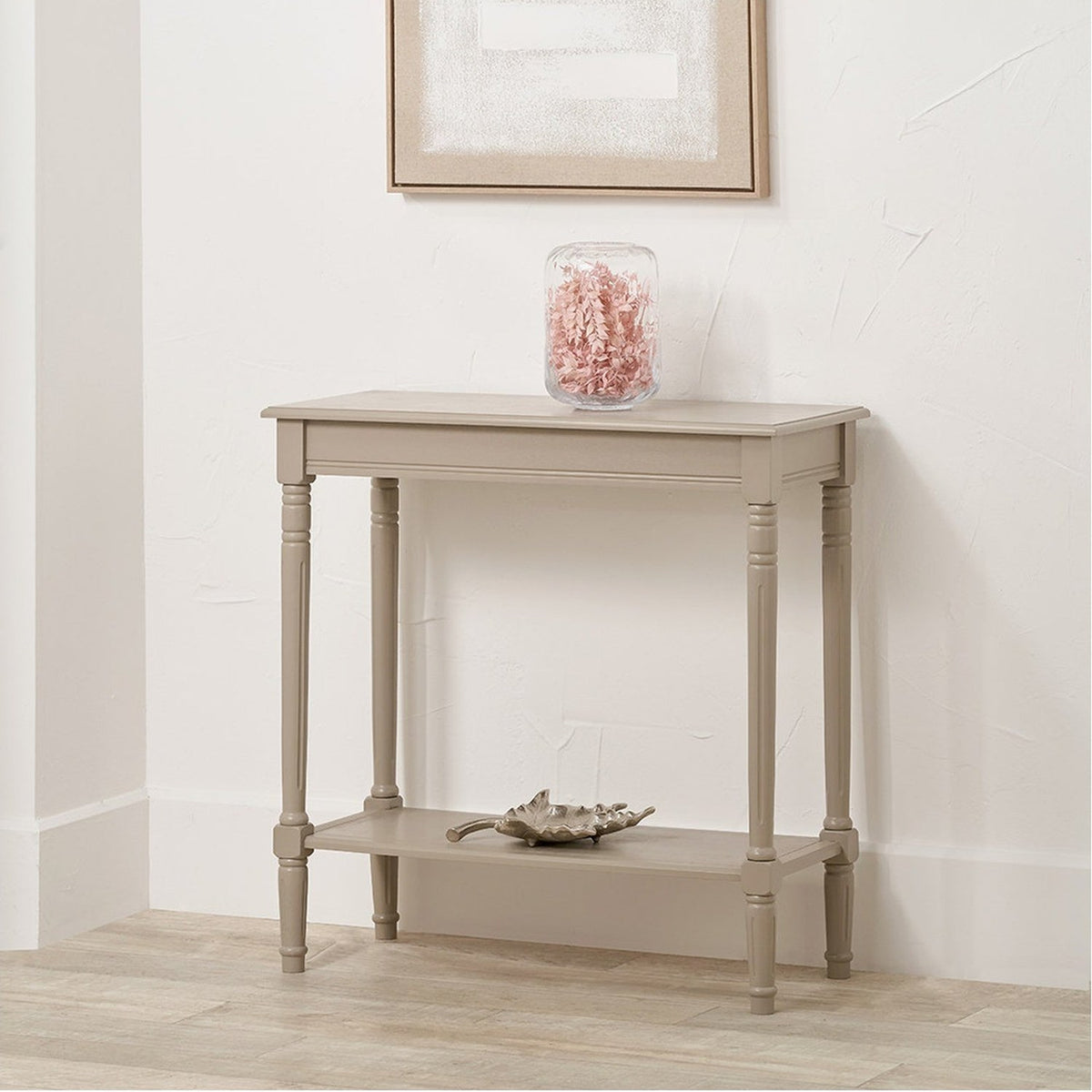 Heritage Putty Pine Console Table with turned legs and lower shelf, shown against a white wall with framed art, glass jar, and decorative dish.