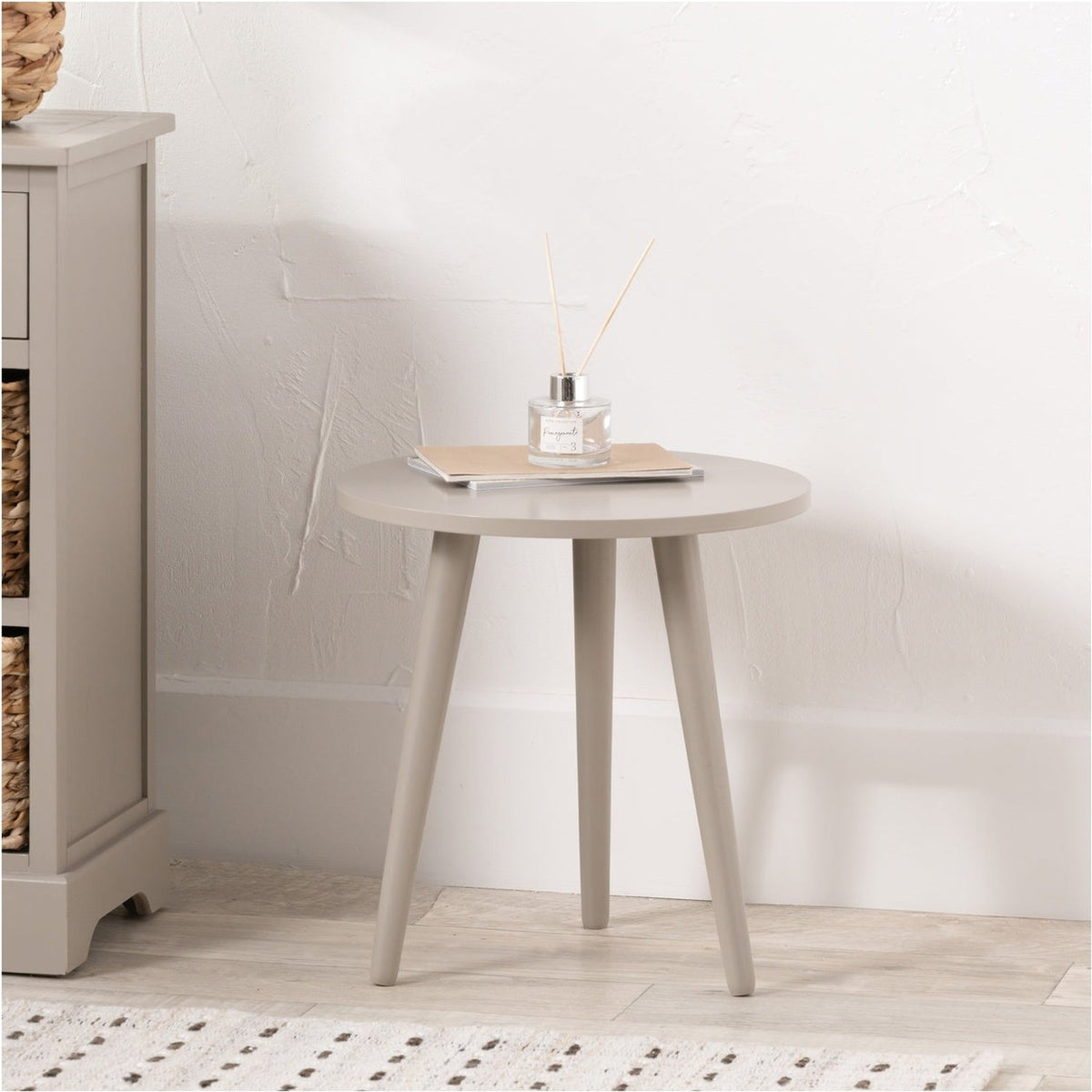 Devonshire Putty Pine Side Table with round wood top and tapered tripod legs in a putty finish, styled with a diffuser and notebook against a light wall.