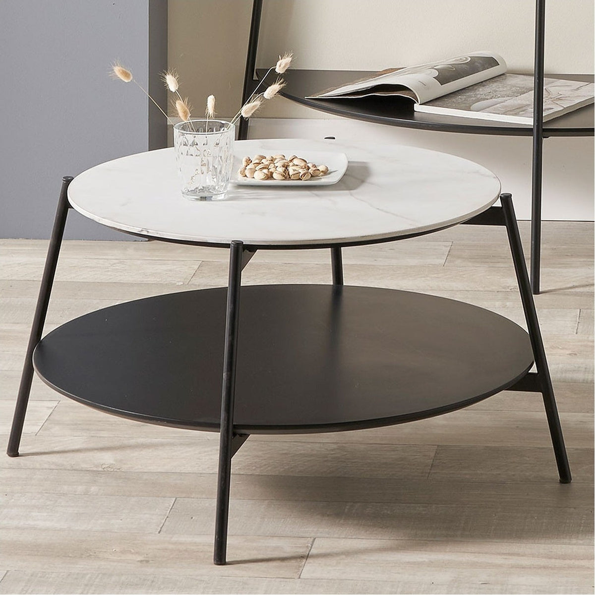 Marchello round console table with white marble-effect top and black lower shelf, both supported by black iron legs, styled with a glass, dried flowers and a snack dish.