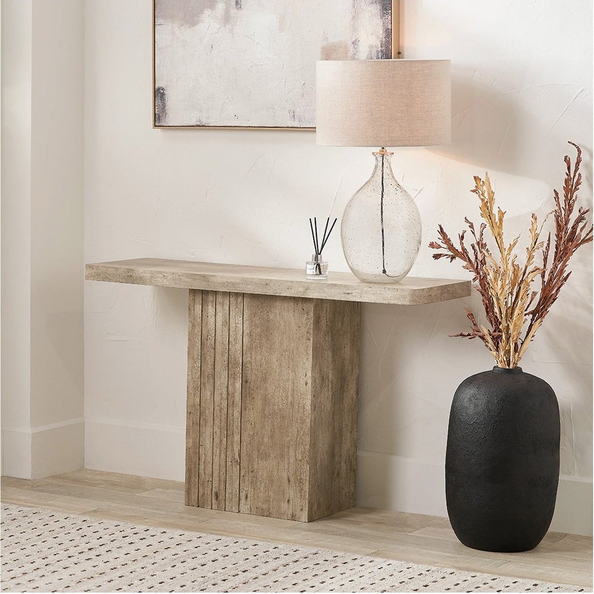 Elkton Concrete Effect Console Table with grooved wood veneer pedestal base, styled in a hallway with a glass table lamp, black vase, and framed wall art.