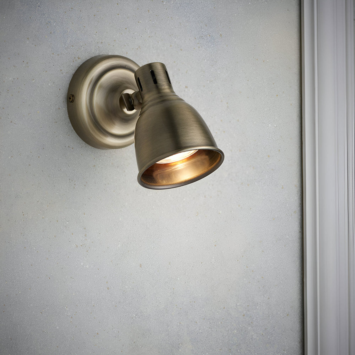 Endon Daneford single spotlight in antique brass with adjustable domed head, mounted on a light wall beside white trim.