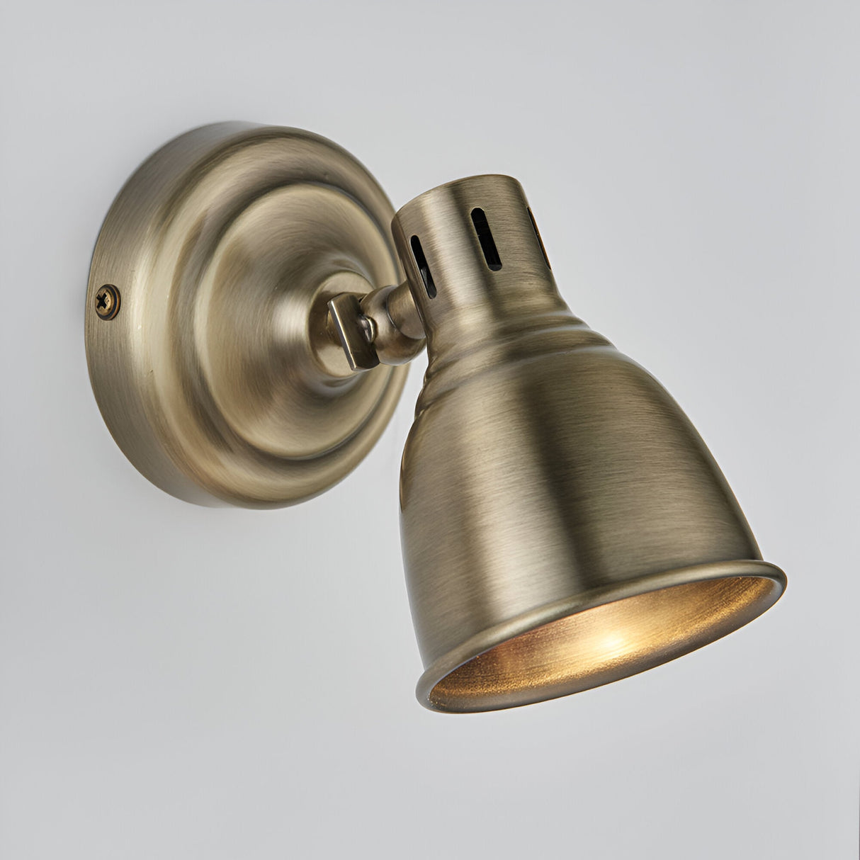 Endon Daneford single spotlight in antique brass, featuring an adjustable domed head on a round wall plate, shown lit against a plain light background.