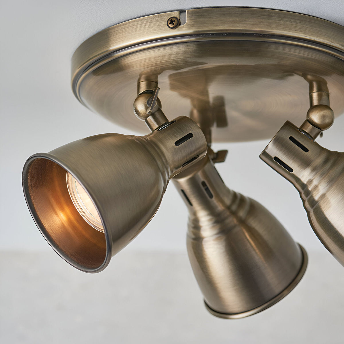 Close-up of the Endon Daneford 3 light round spotlight in antique brass, showing adjustable steel heads on a circular ceiling plate.