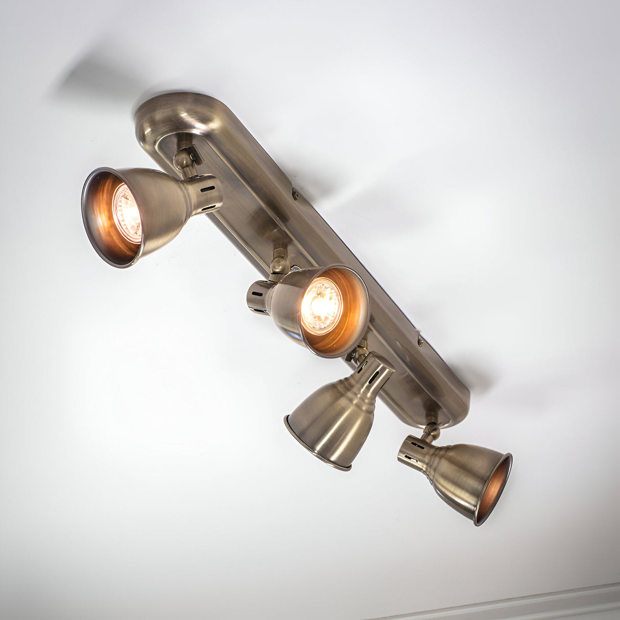 Endon Daneford 4 light spotlight in antique brass, ceiling-mounted with four adjustable heads on a linear plate, two lit, viewed from below.
