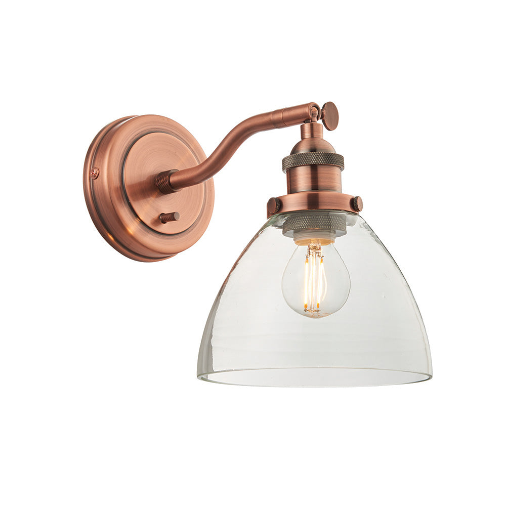 Endon Wentworth wall light in copper with adjustable knuckle, toggle switch and clear glass dome shade over a lit E14 filament bulb, on white.