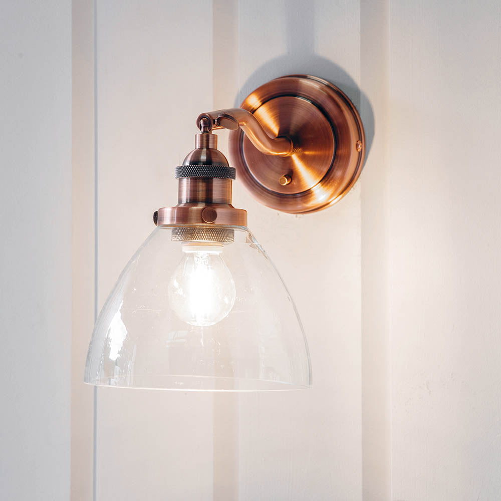 Endon Wentworth wall light in copper with adjustable knuckle, knurled lamp holder and clear glass dome shade, mounted on a white panelled wall.
