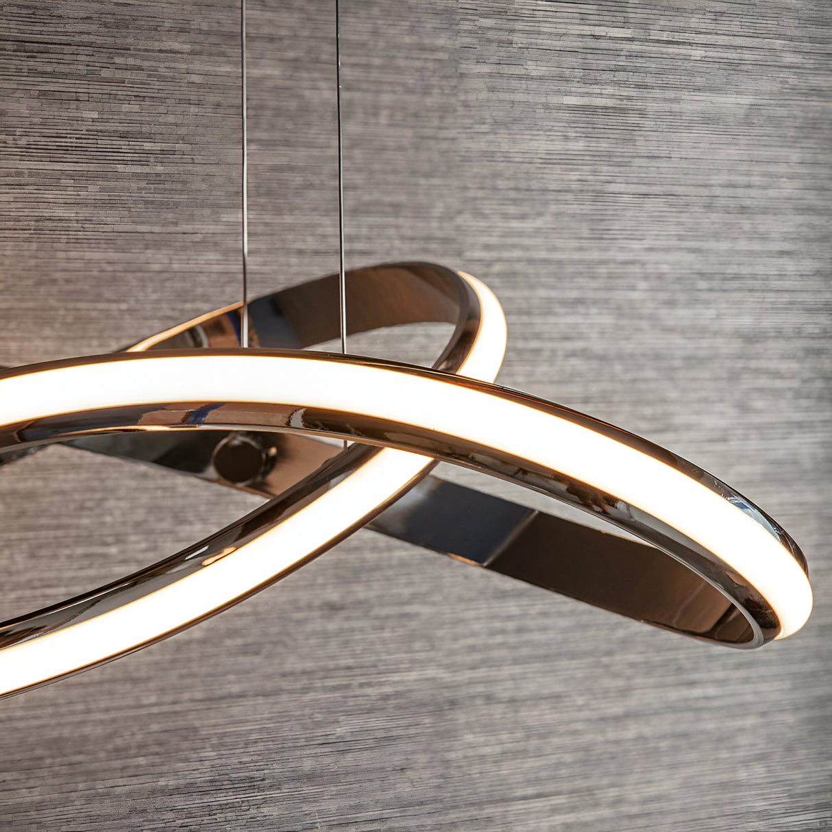 Close-up of Endon Neve pendant light in chrome, showing the looped sculptural band with a white LED diffuser, suspended by thin wires against grey wall.
