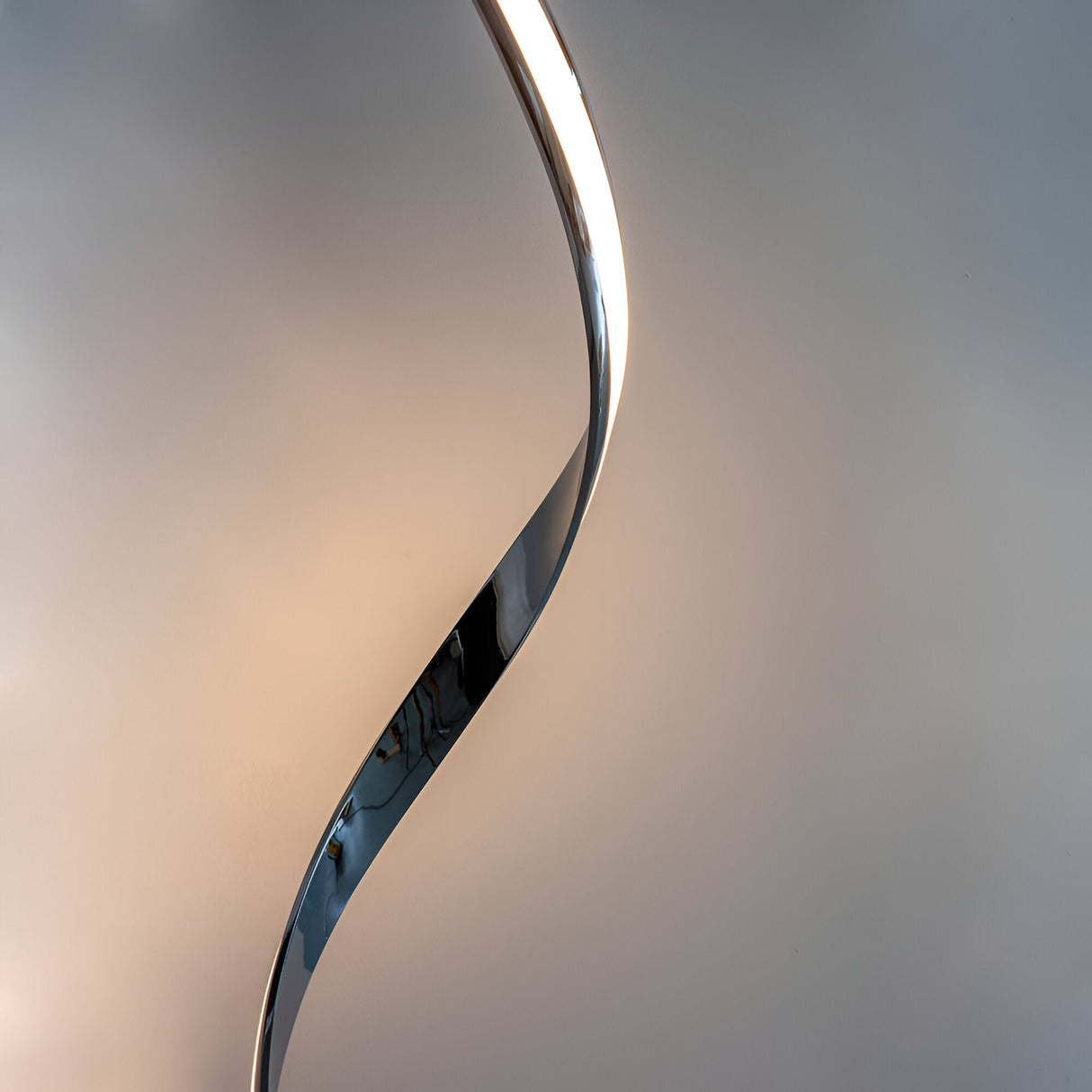 Neve Floor Lamp in polished chrome with a sculptural curved form and illuminated white diffuser, shown against a plain light background.