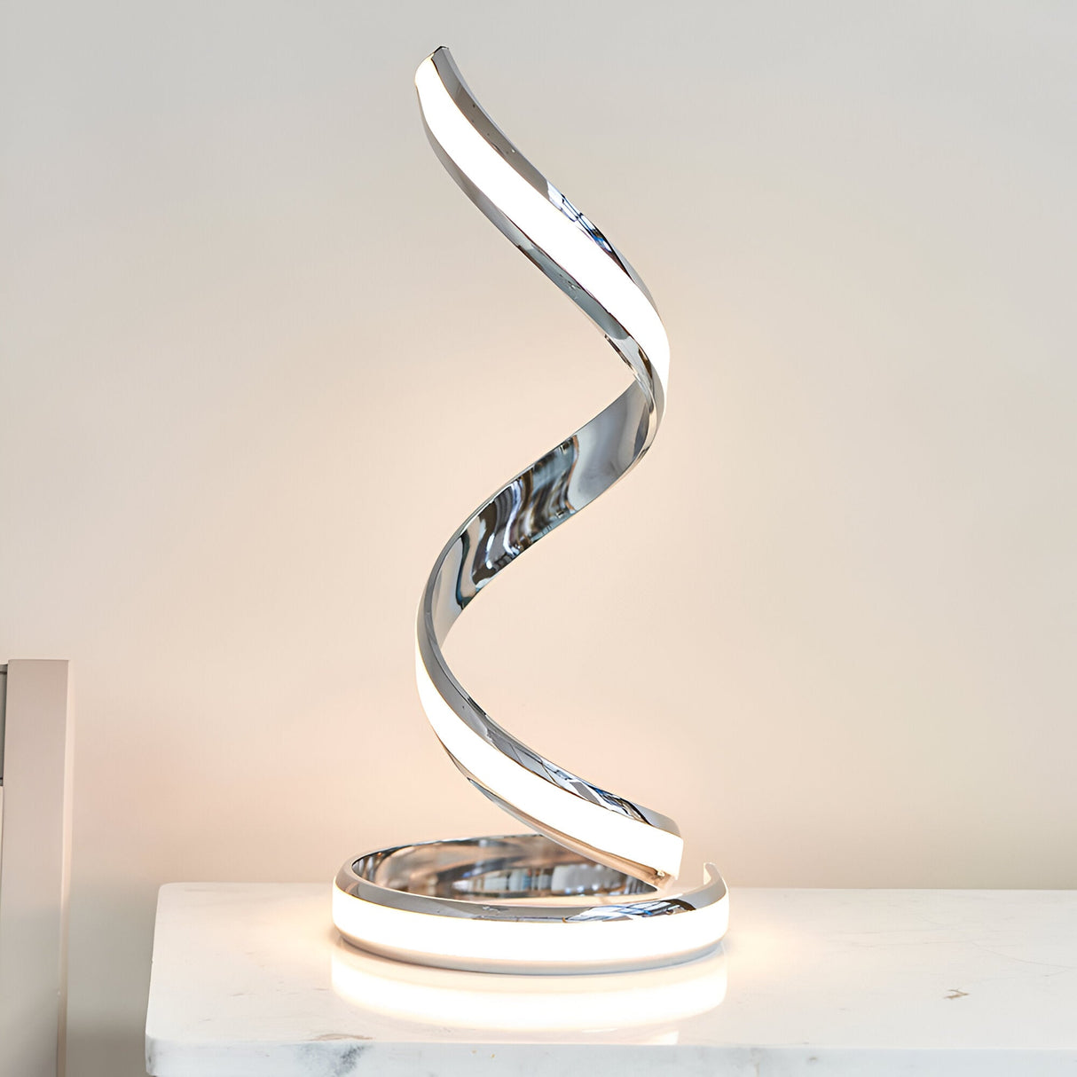 Endon Neve table lamp in polished chrome with a spiralling sculptural form and integrated LED diffuser, shown on a white marble surface.